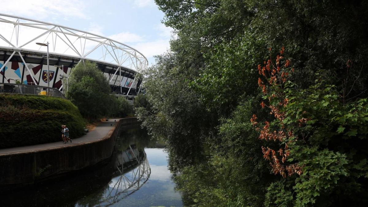 A scenic river view, runners on a pathway along side it. A stadium in the background.