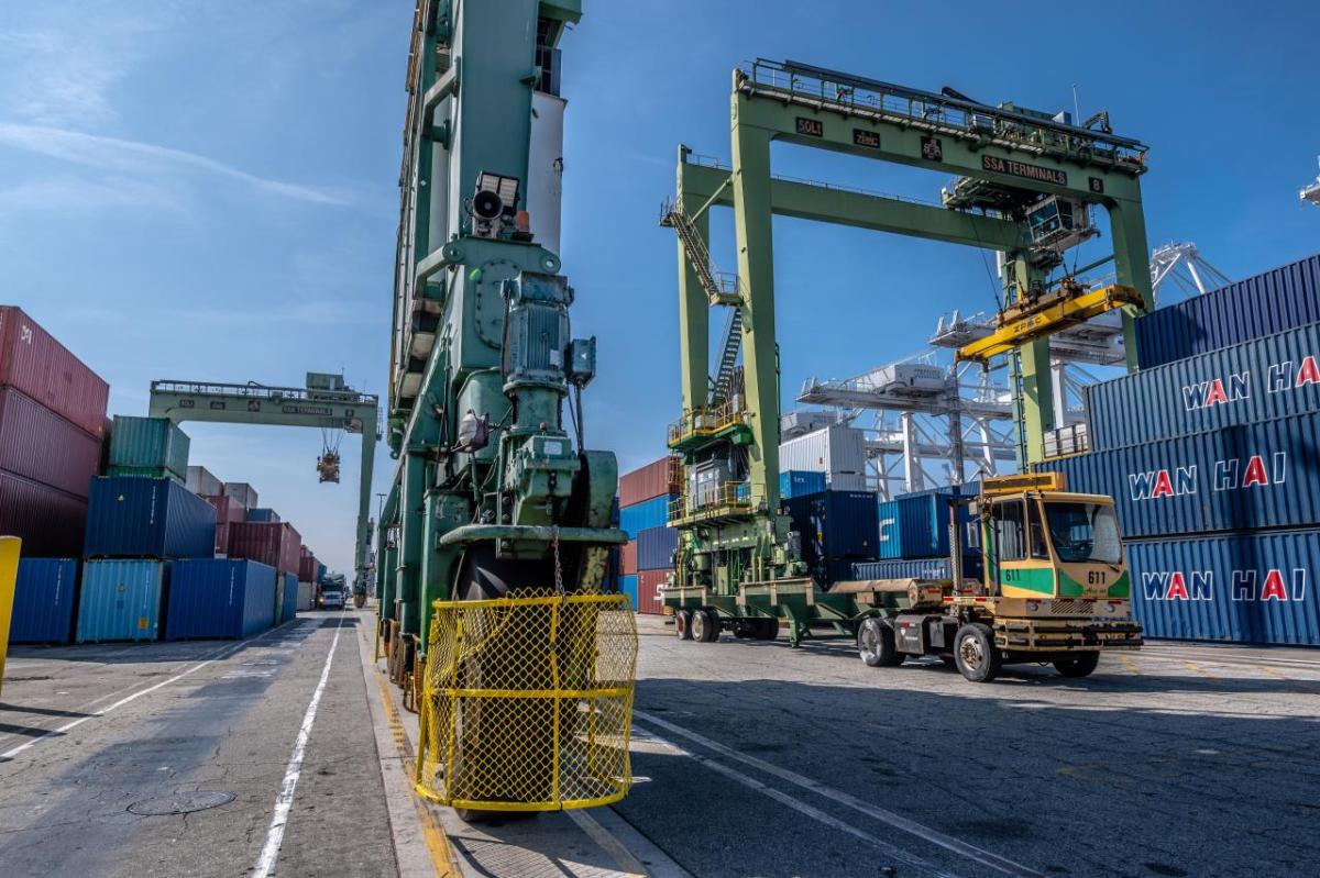 Crane truck moving along stacks of shipping containers.