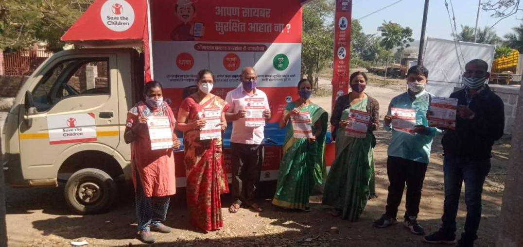 a group of adults standing in front of a van with "save the children" logos on it. Each person holding a poster from Save the Children