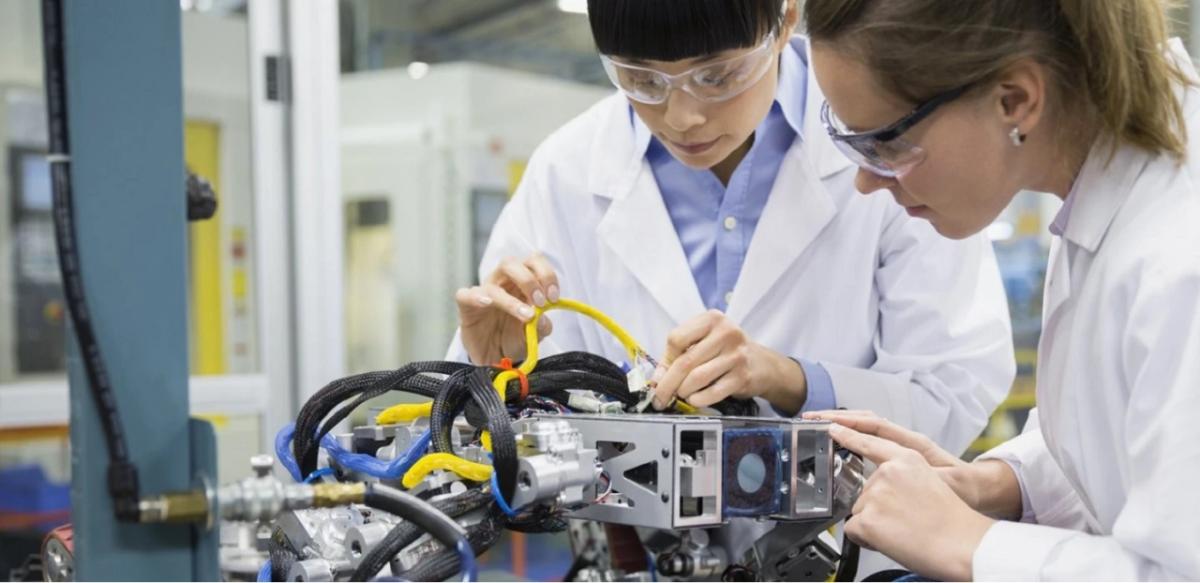 two people wearing lab coats and safety glasses working on a piece of equipment