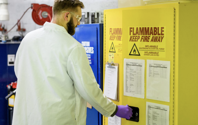 A person opening a yellow locker that has a fire hazard sign on the front of the door 