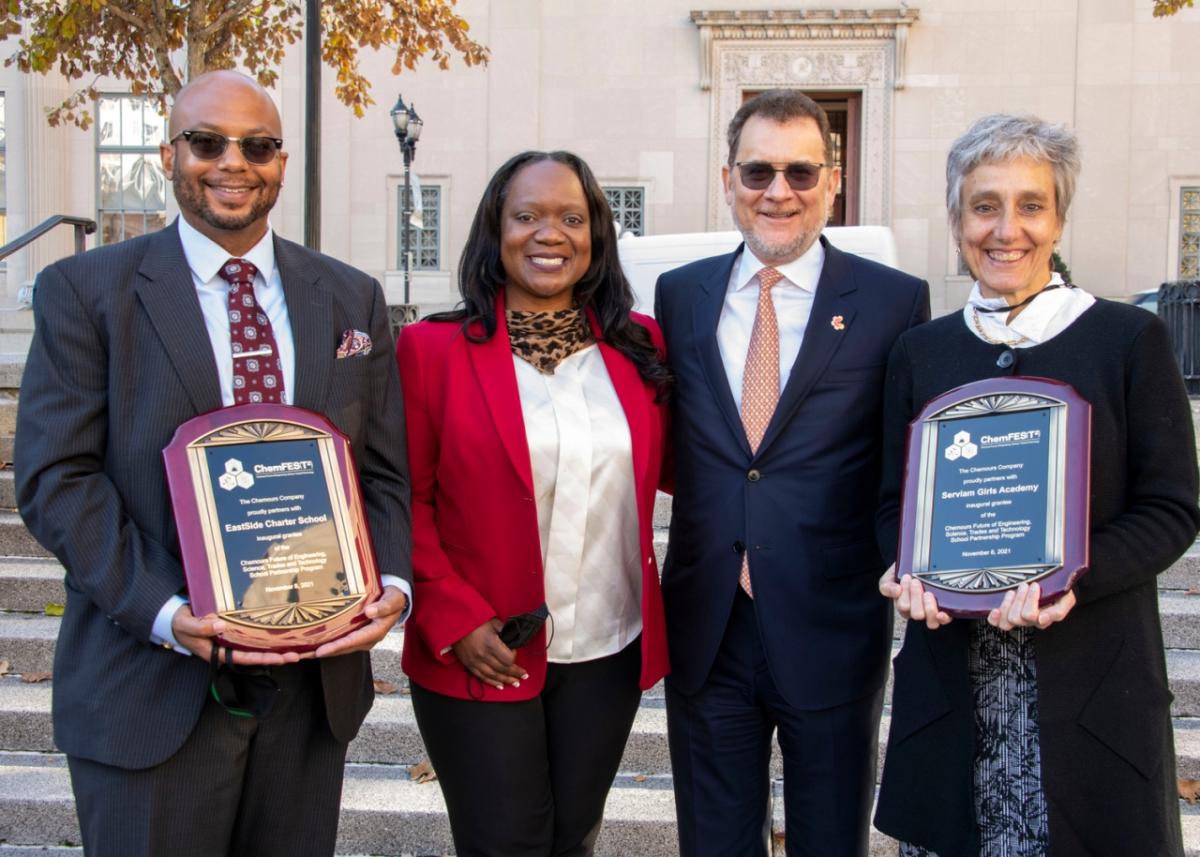 four people in business attire standing outside, holding plaques