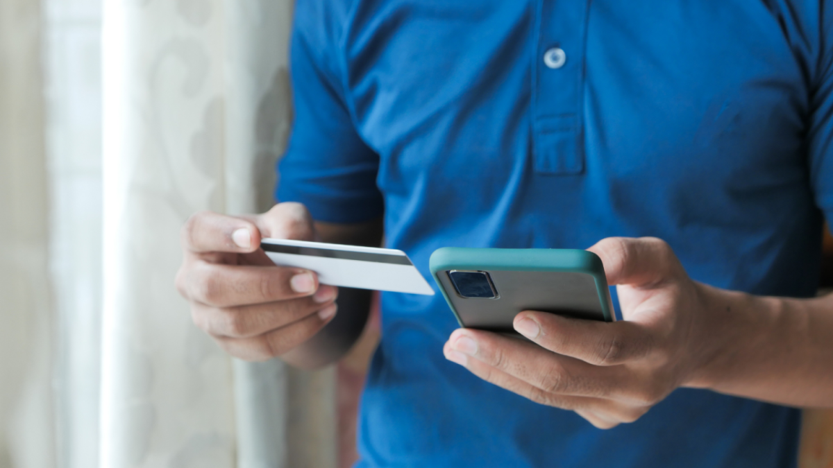 A person holding a credit card in one hand and using a cell phone with the other.