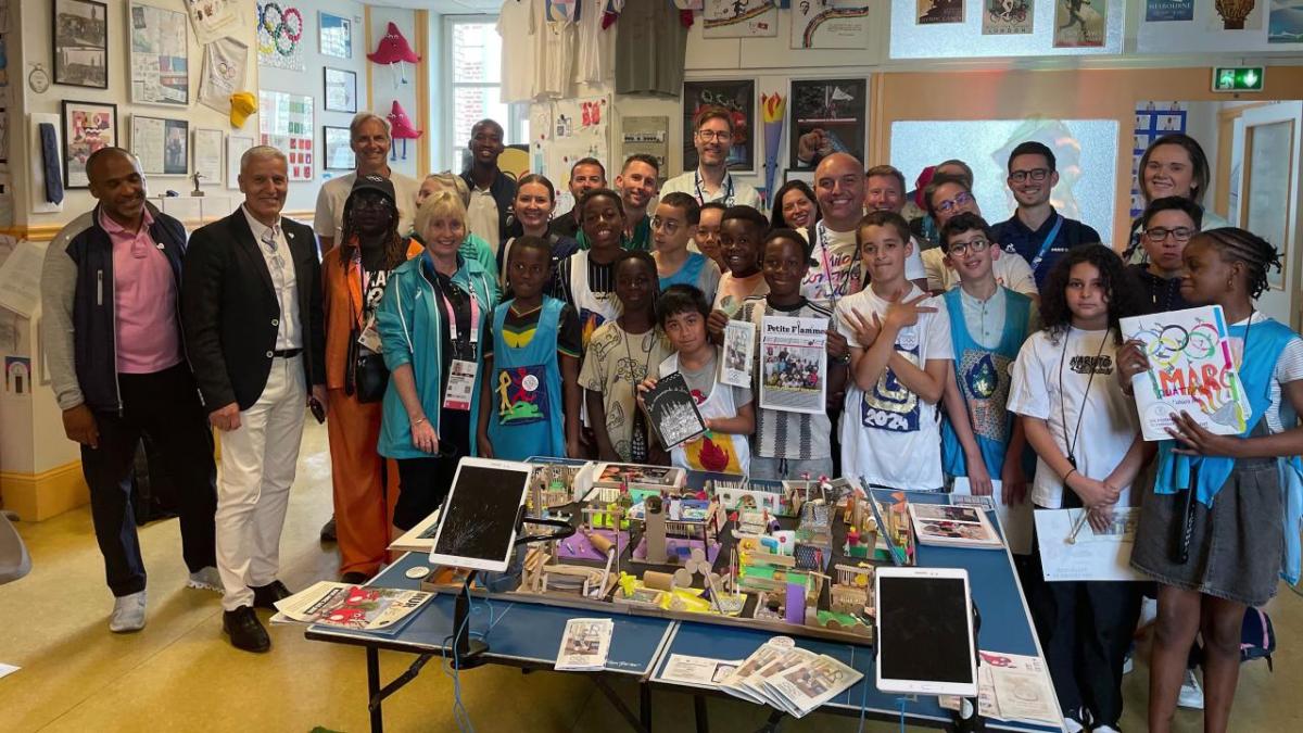 A large group photo of staff and students stood around a crafts table 