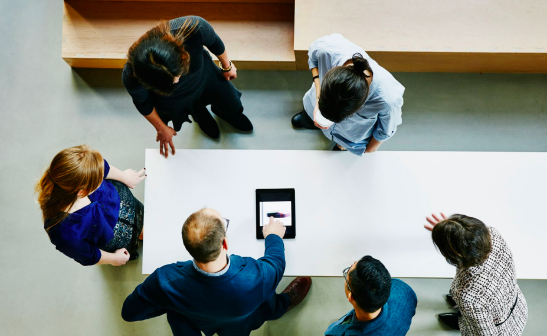 overhead view of group of workers at a table working with a tablet