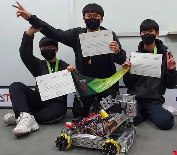 3 students kneeling behind a robot