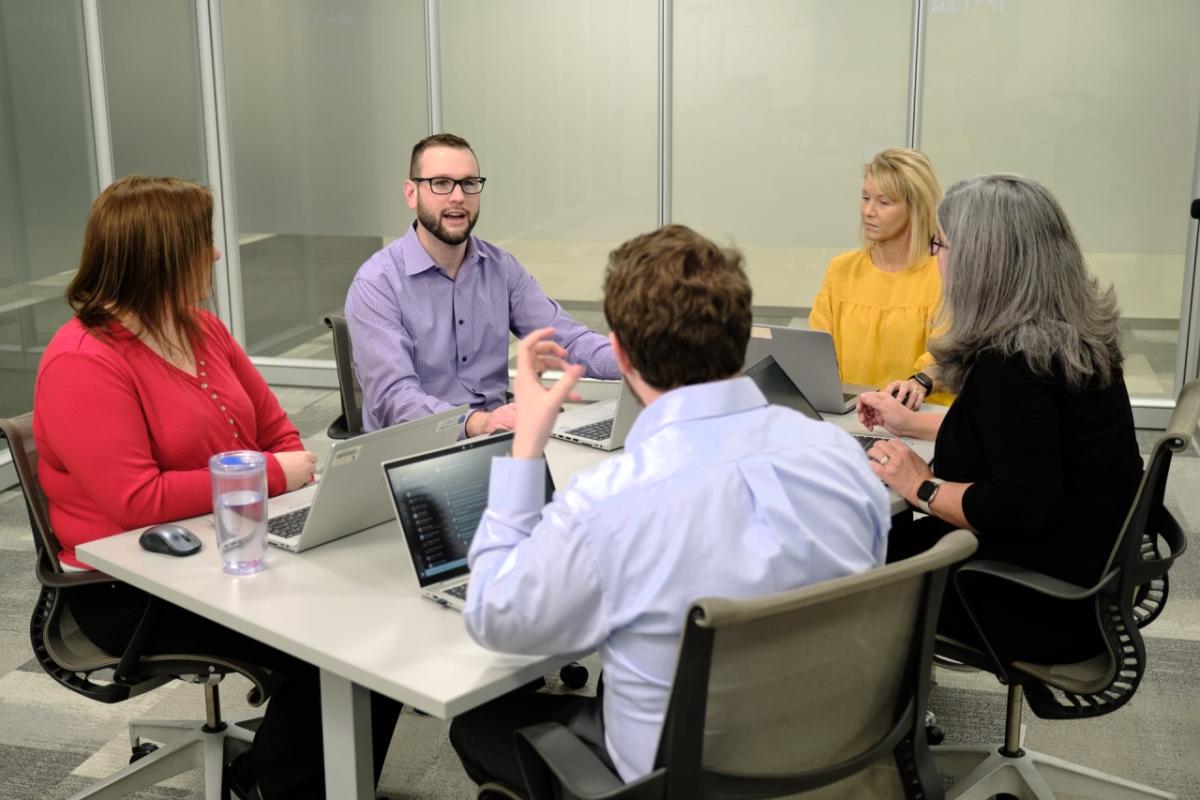 Richard McMichael, in a light purple shirt, at a conference table talking to coworkers