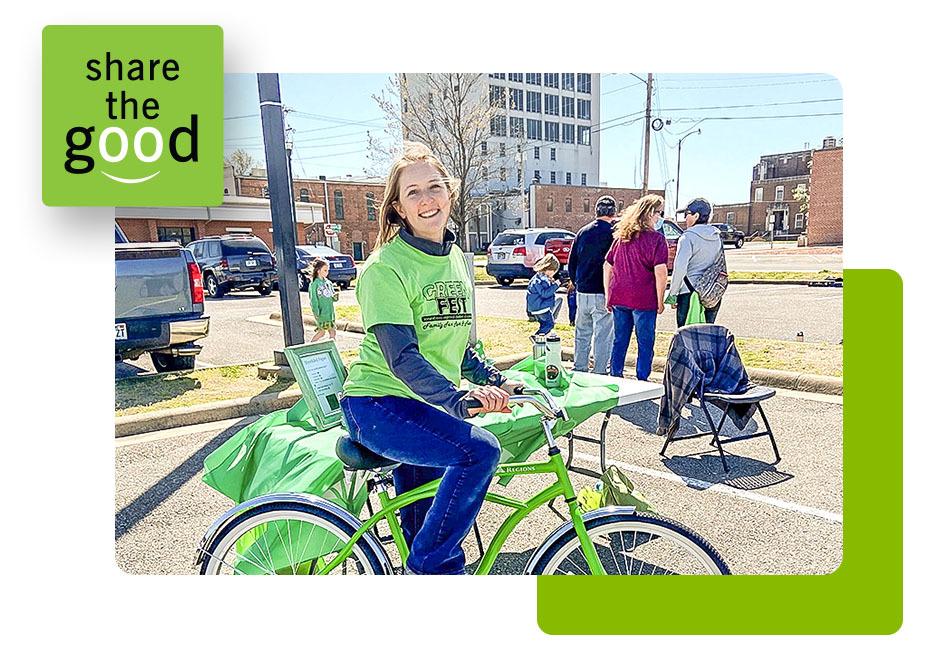 Shelly Gist on a green bicycle next to a table outdoors.