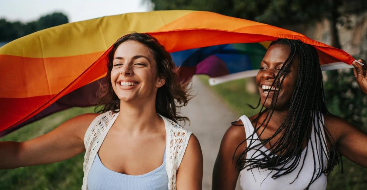 Two people smiling holding up the LGBTQ+ flag