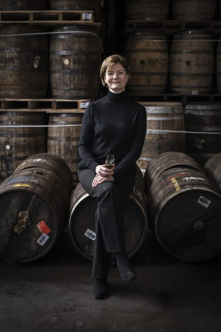 Stephanie MacLeod seated on a barrel, many barrels behind her.