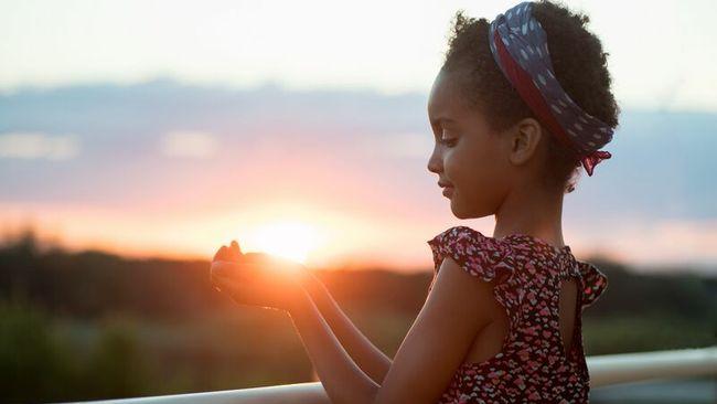 Photo of a child holding their hands out while the sun sets