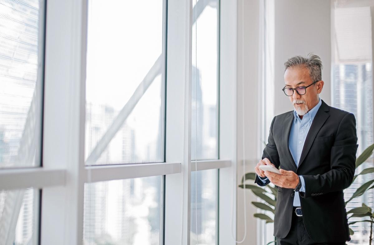 A person standing by a glass window looking at their phone.