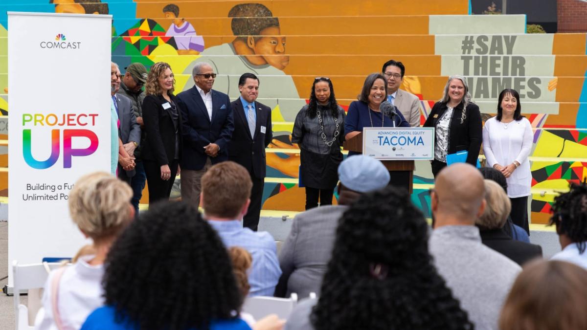 Mayor Victoria Woodards at a podium, others behind them and bleachers in the background. Audience seated in front.