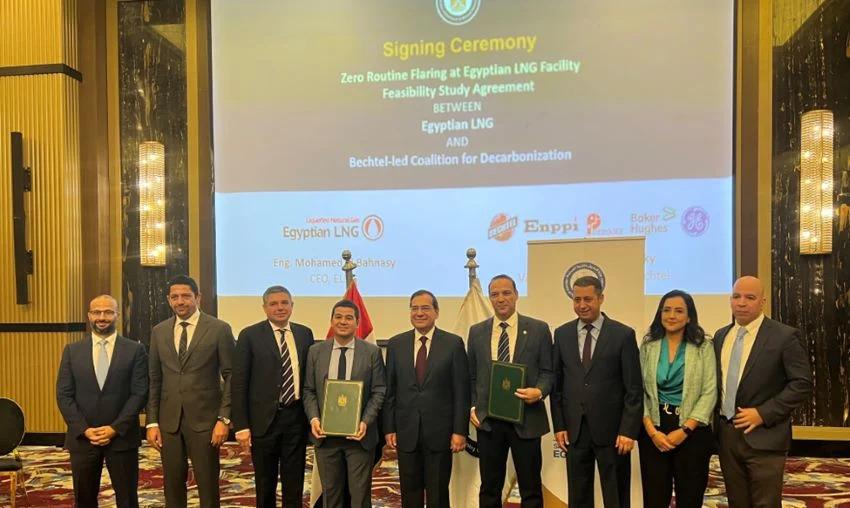 A line of people at a "signing ceremony" Some holding official documents. A large screen behind them.