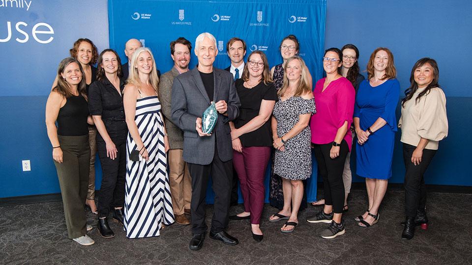 Group standing together at award ceremony, one person is holding out the award