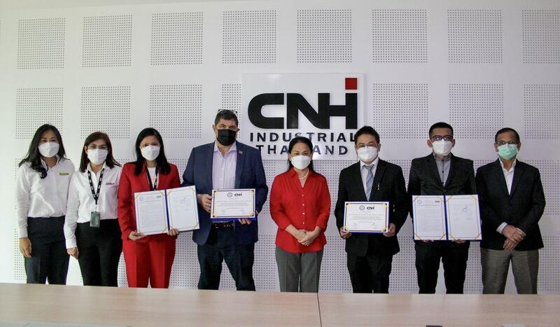 Group of people, all wearing protective masks, stand in front of CNHI sign in a conference room. Some hold documents