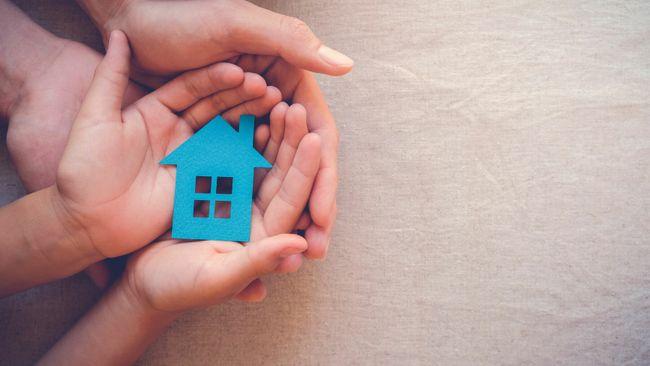 Someone holding a very small blue house in the palm of their hands