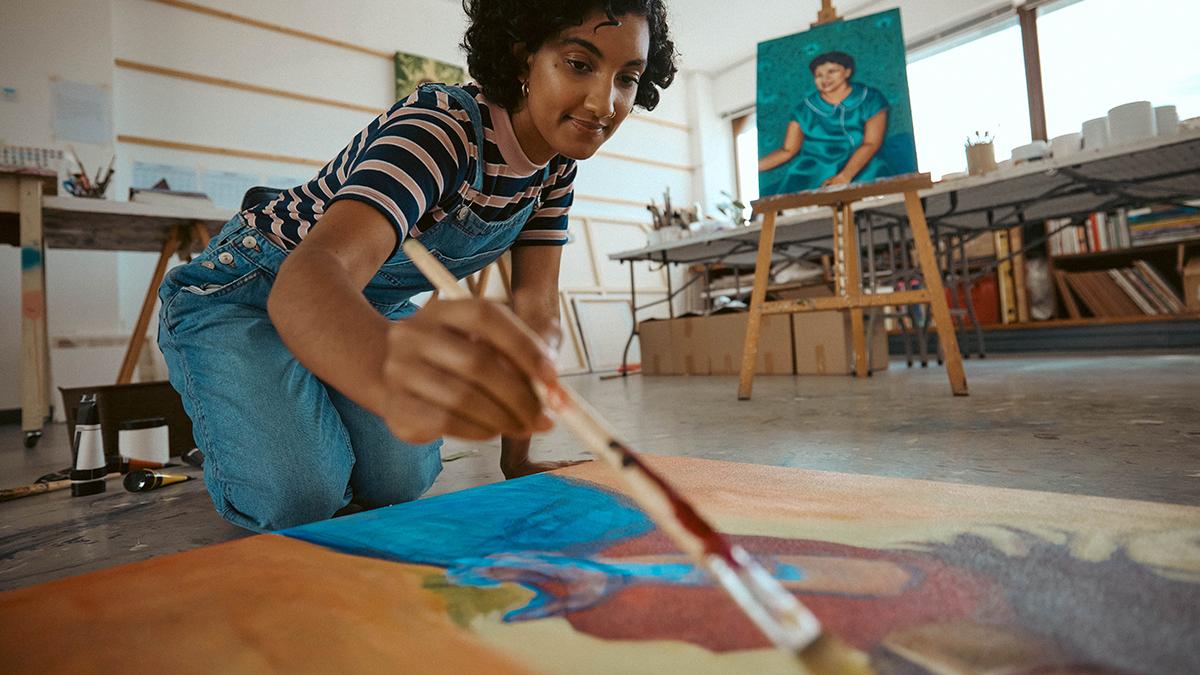 Young adult in art studio holding a paintbrush and getting ready to work on a large painting canvas.