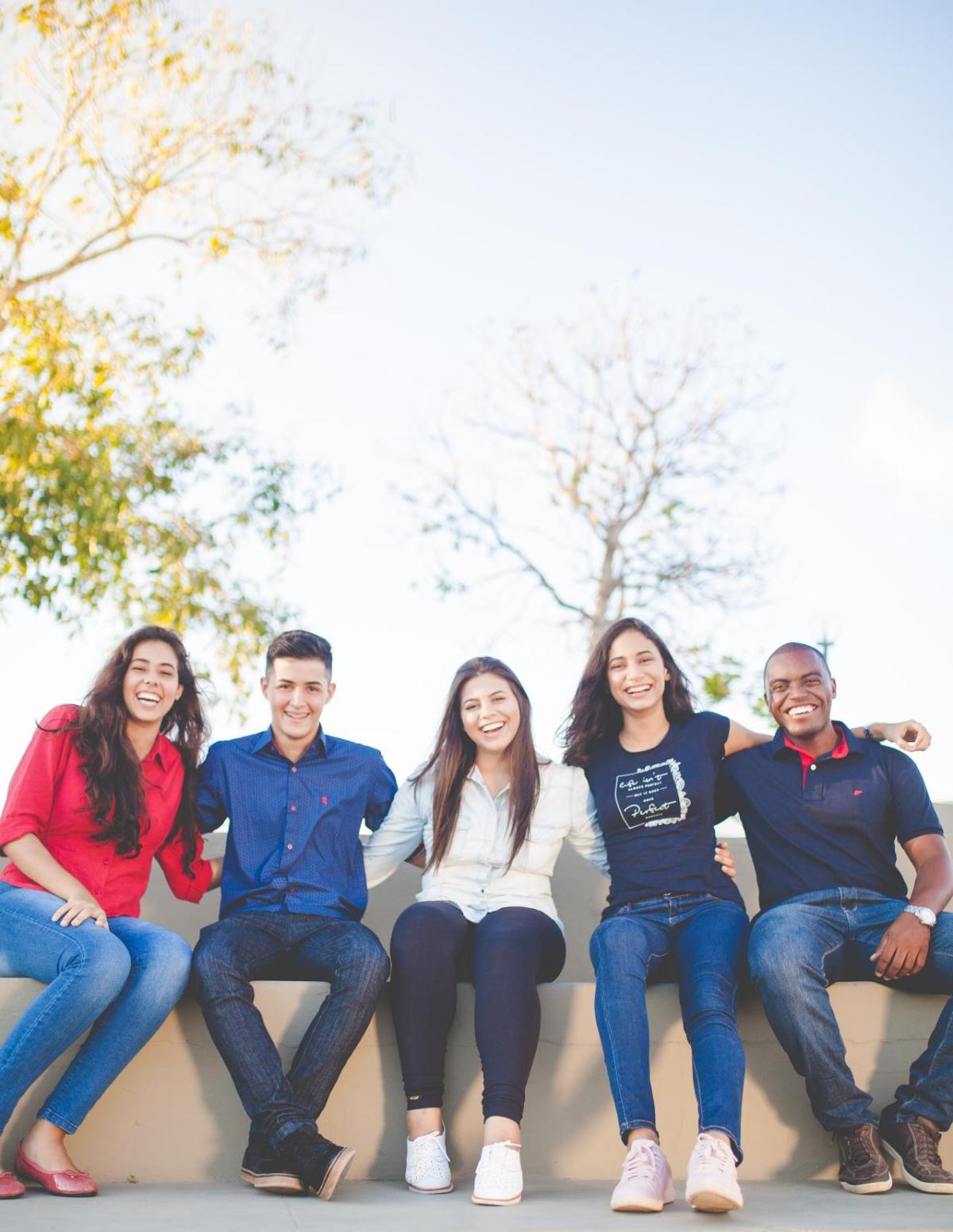 A group of five people sitting on a bench with arms around each other.