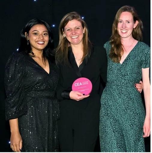 three people with arms around each other. The center person holding the CEA award