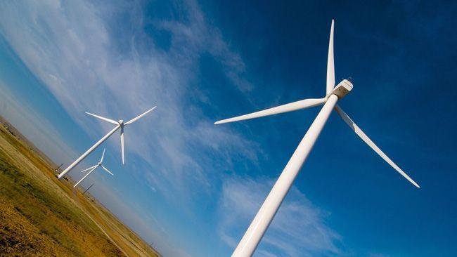 Angled shot of a row of wind turbines against a blue partly cloudy sky.