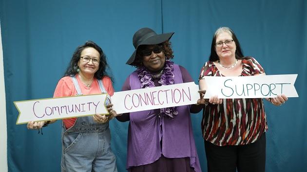 Three people holding signs with the words "Community, Connection, and Support" on them.