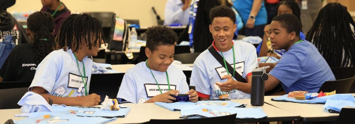 A group of kids in matching shirts talking and smiling, seated at a long table.