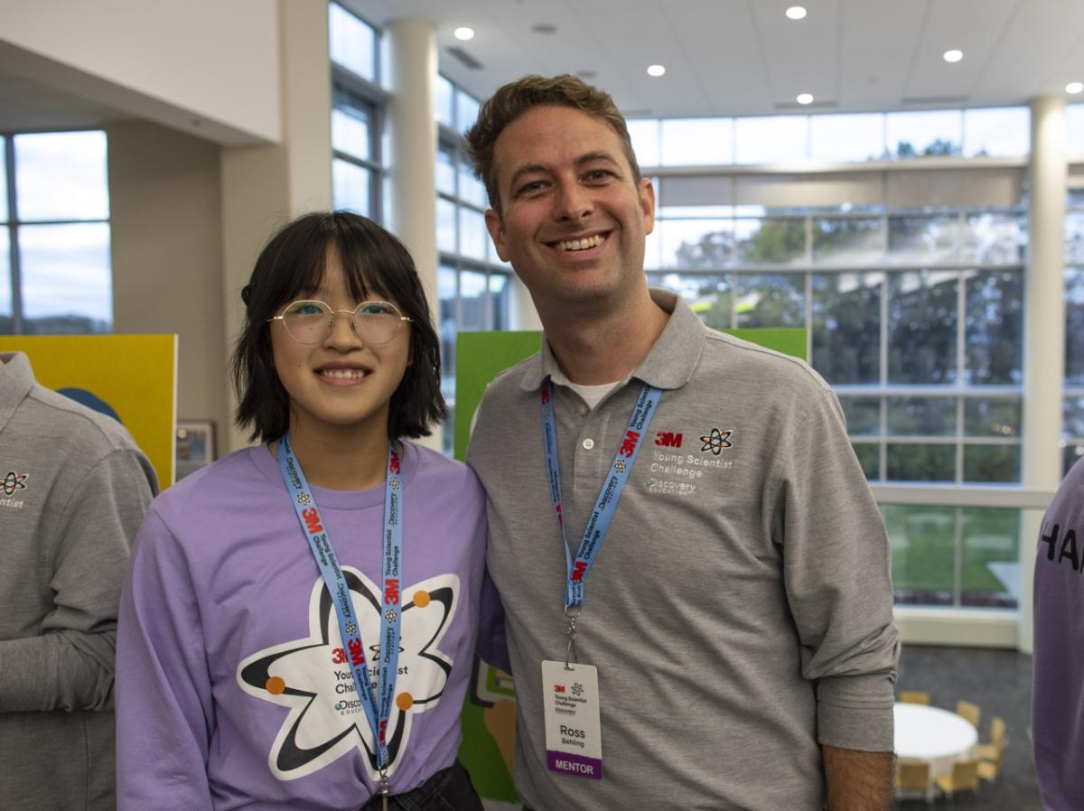 A student and adult stand next to each other. Both wearing 3M youth scientist t-shirts and lanyards..