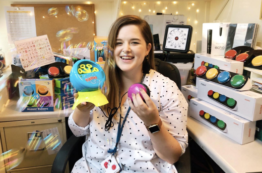 A person holding up a bubble machine and colorful button, colorful products on a desk behind them.