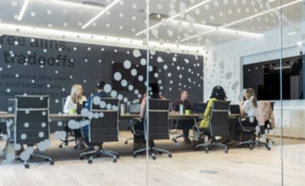 Through clear glass walls, people seated at a conference table.