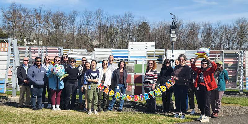 A group posed outside holding a banner "Happy Birthday".