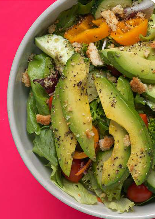 Close up of a bowl of sliced Avocado and other vegetables and seasonings