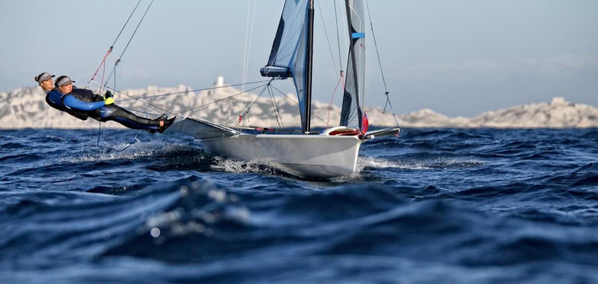 Two people leaning far out of a sailboat on open water.