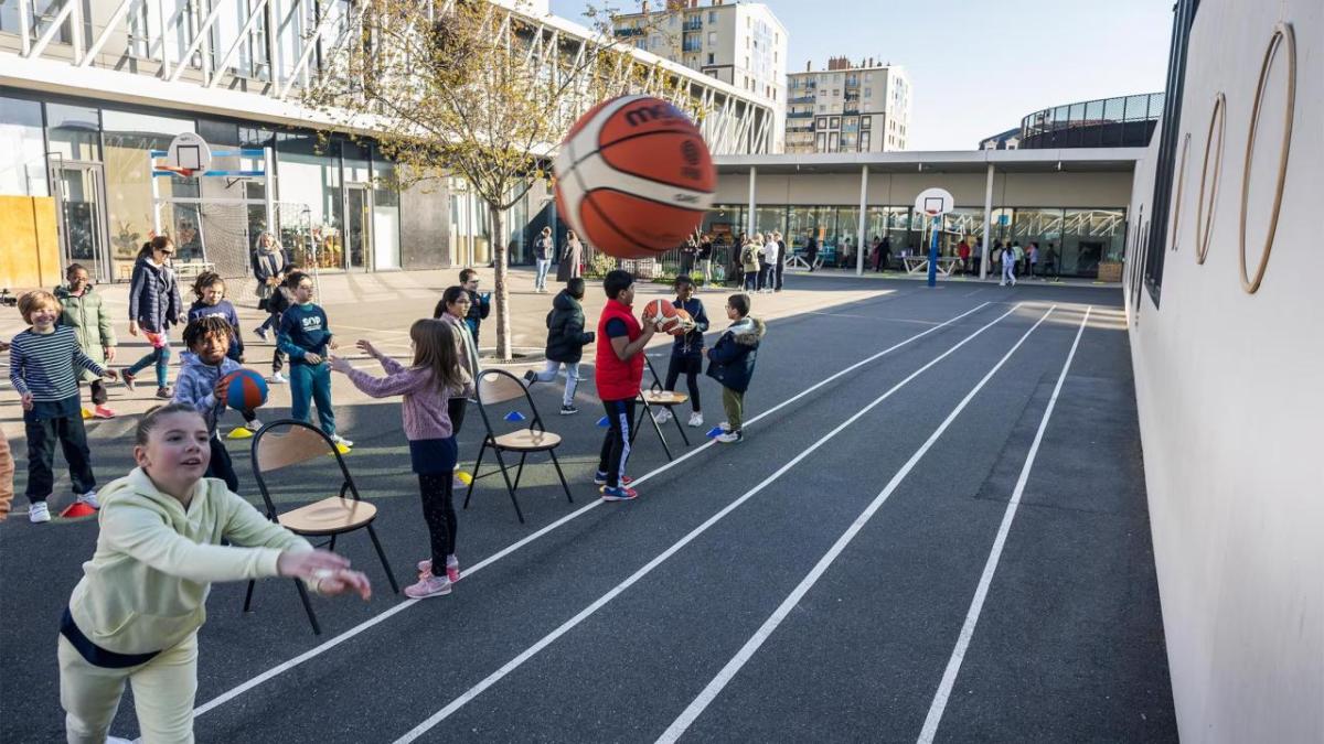 Children outside throwing basketballs against a wall.