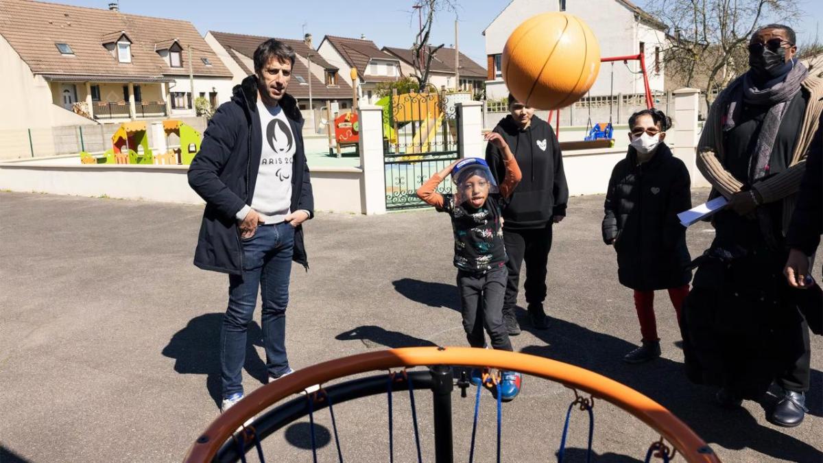 A child throwing a basketball as adults watch.