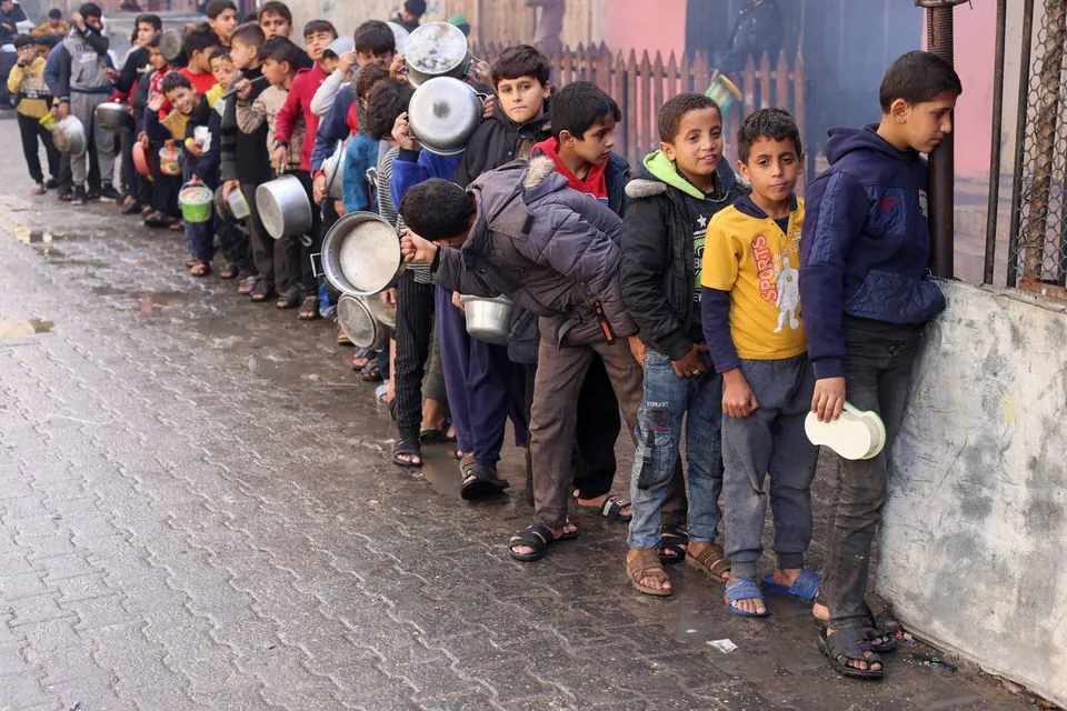 Palestinian children carry pots as they queue to receive food cooked by a charity kitchen, amid shortages in food supplies, as the conflict between Israel and Hamas continues, in Rafah in the southern Gaza Strip December 14, 2023./ Photo by Saleh Salem for Reuters. 