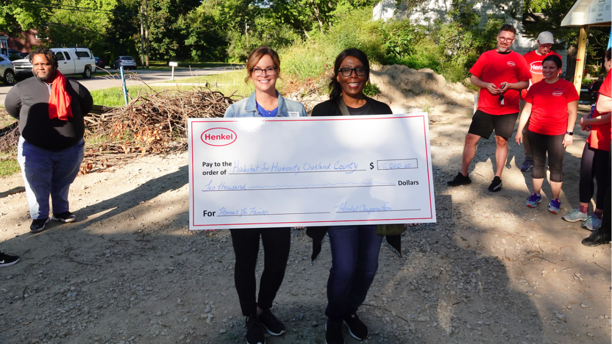 two people holding a large check made to Habitat for Humanity. Crew of volunteers behind them.