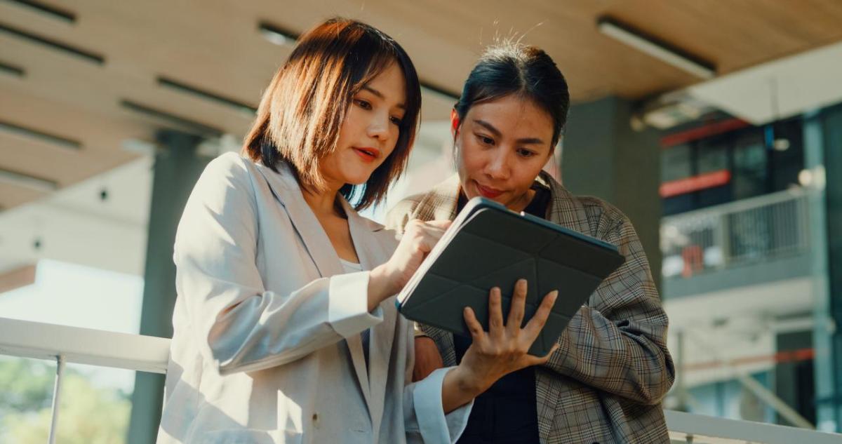 Two standing people looking at a tablet device in a business setting.