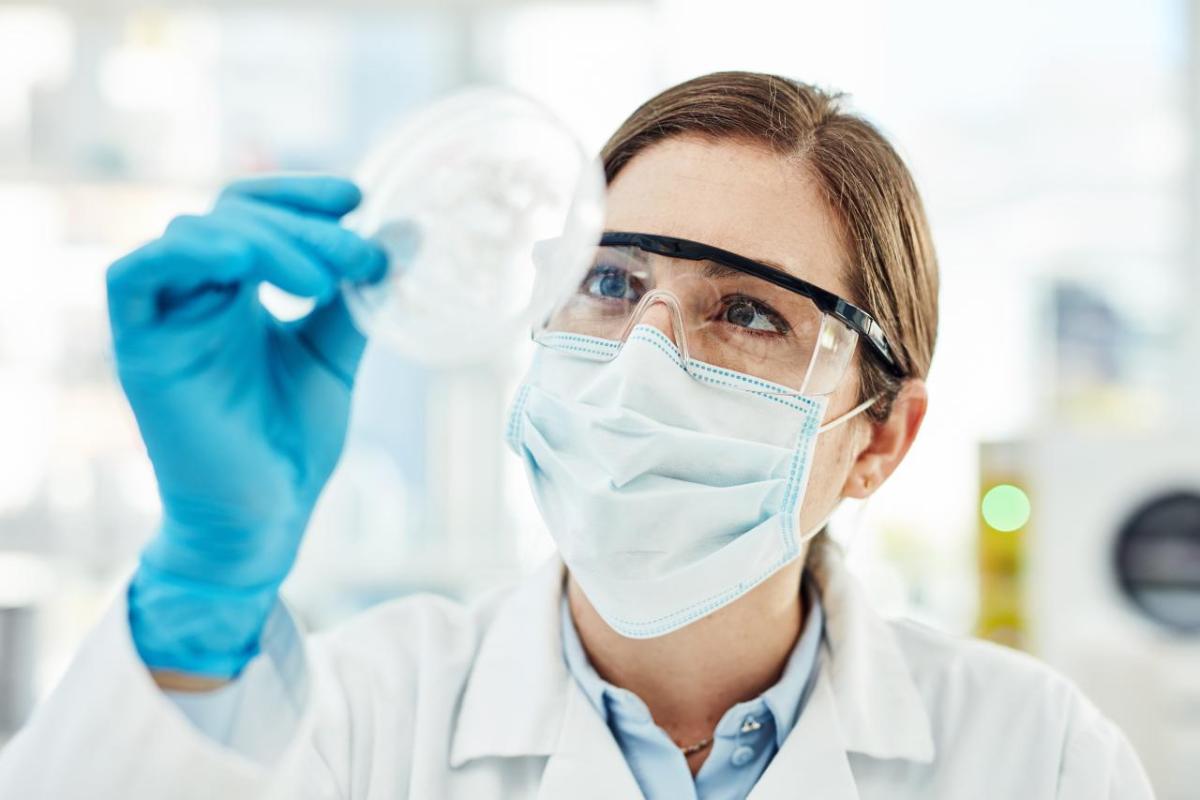 A scientist in protective gear looking at a petri dish