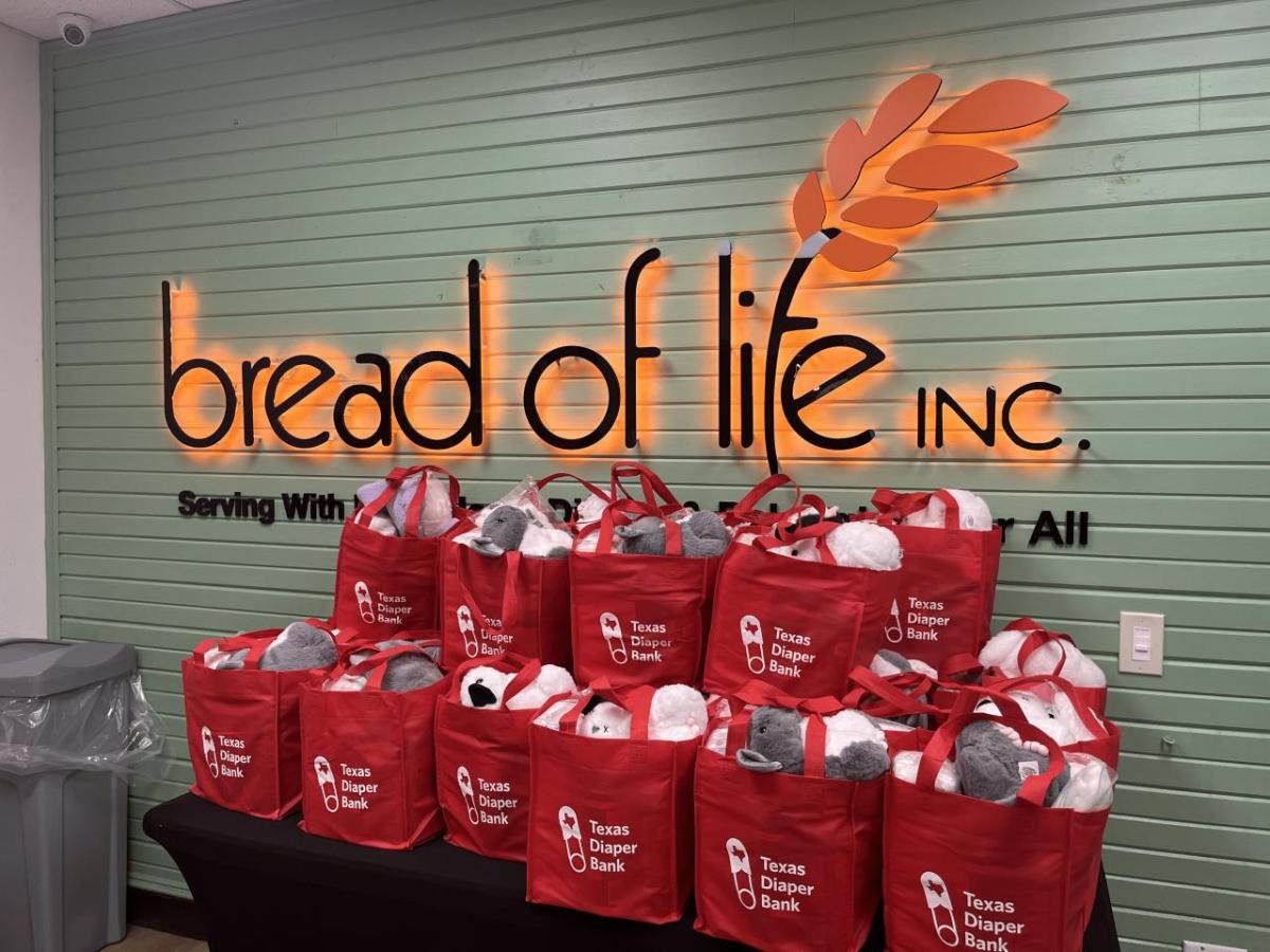 "bread of life" sign on a wall behind a table of filled red bags.