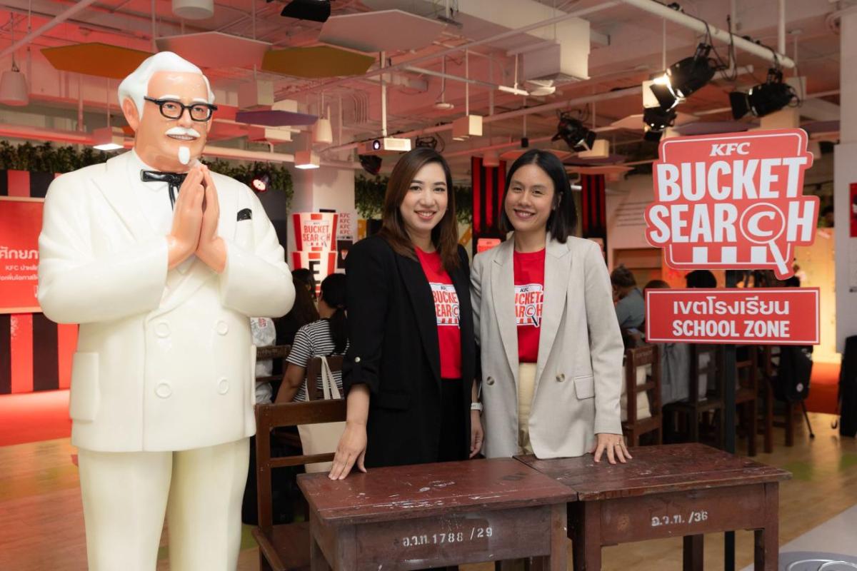 Two people in matching shirts standing behind a desk, next to a large statue of a person.