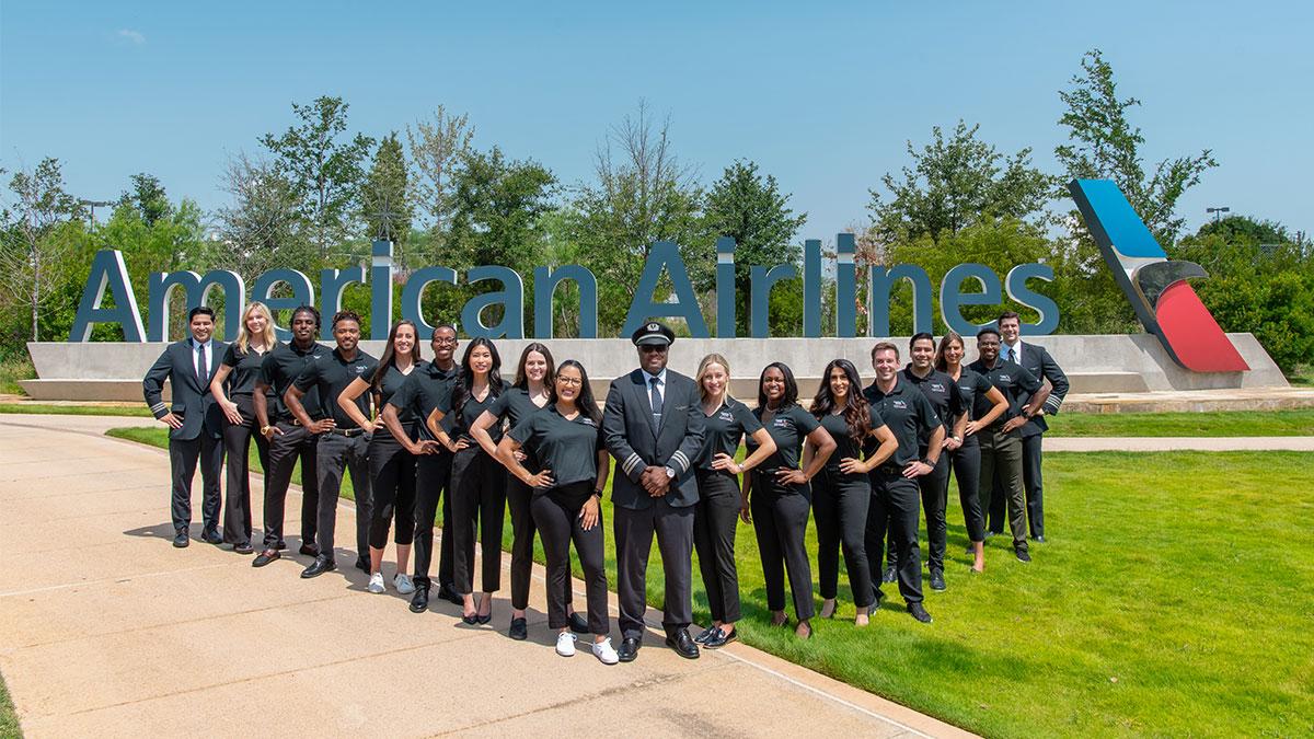 Group posed outside in a "V" formation. American Airlines sign behind them.