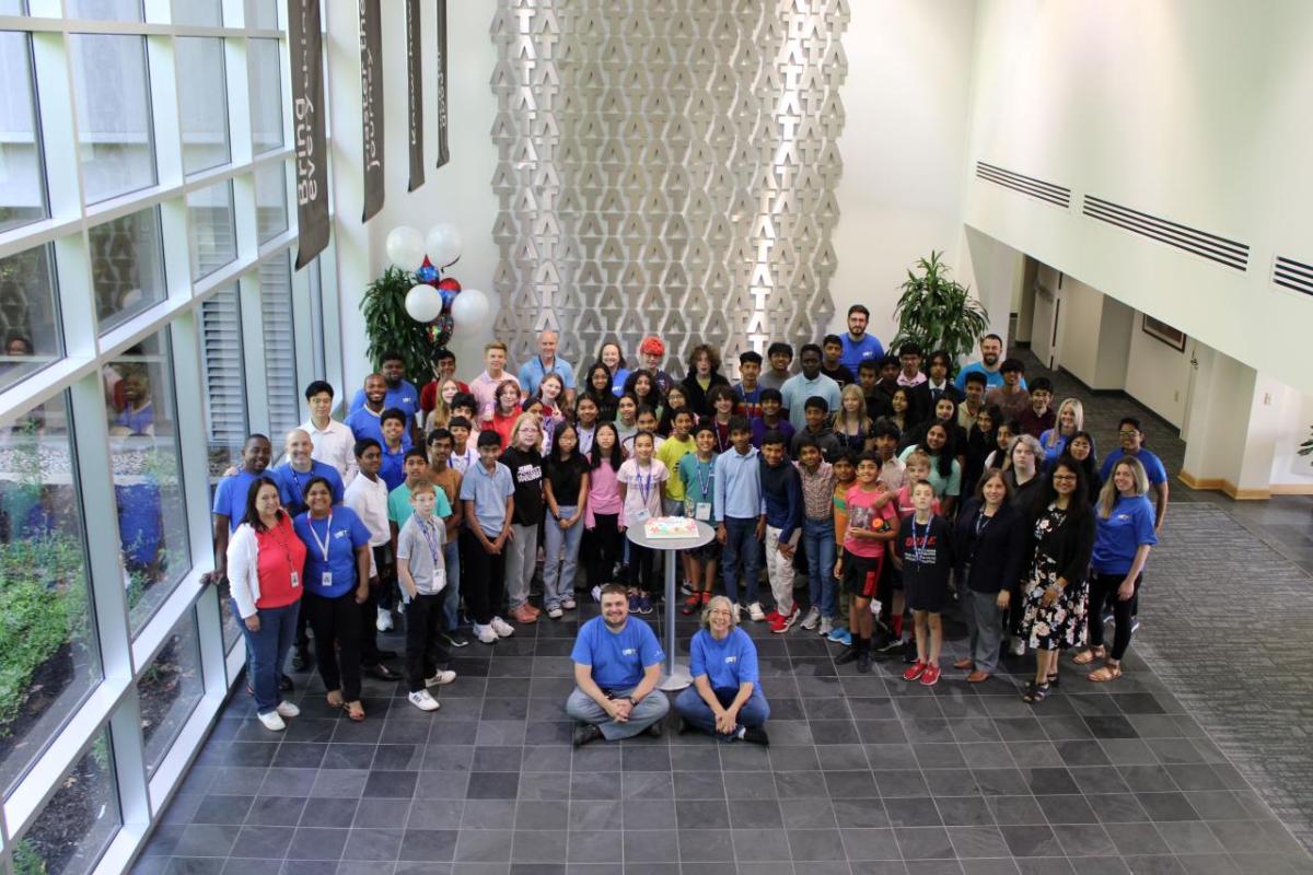 Wide view of a group of adults and children in an open area in a building.