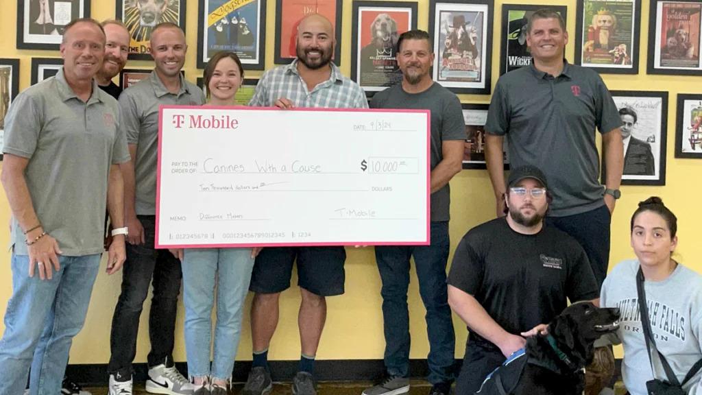 A small group posed with a large check in front of a wall of pictures.