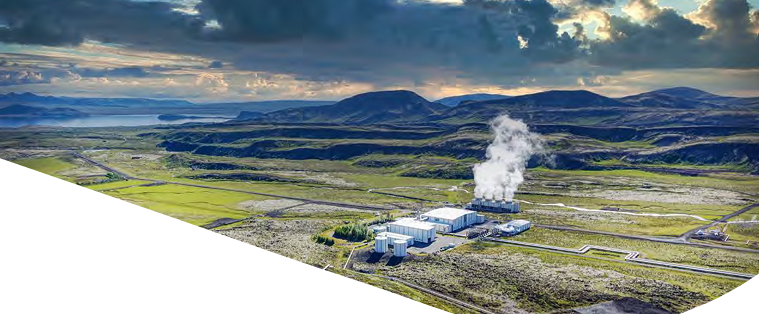 Aerial view of a hilly landscape. Large buildings and roads to them are central in an open grassy area. Steam coming from one area.