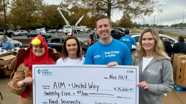 Four people smiling and holding up an oversized check, one in a chicken costume