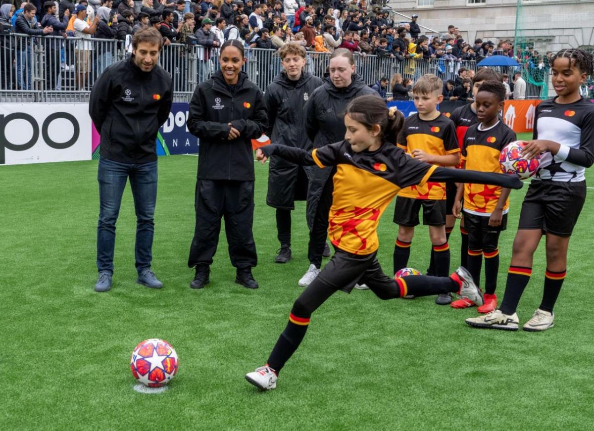 Adults look on as a child kicks a soccer ball.