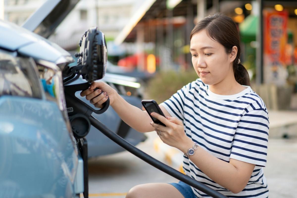 a person looks at their phone while plugging in their vehicle