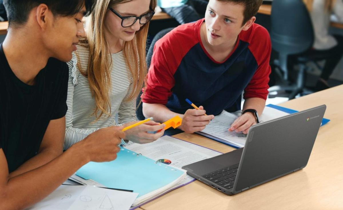 Students working together at a desk, an open laptop between them.