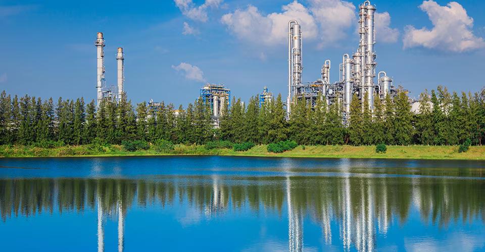 industrial buildings beyond a treeline and pond